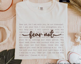 Op de afbeelding: Ivoor Comfort Colors T-shirt met de woorden "Fear not" in een cursief lettertype. Het shirt heeft een gedrukte passage uit Jesaja 41:10-13. De tekst is donkergrijs.