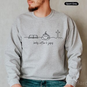 May include: Sport Grey sweatshirt with a black line art design featuring an open book, a coffee cup, and a cross, with the words "books, coffee & jesus" below. The sweatshirt is a solid light gray color.