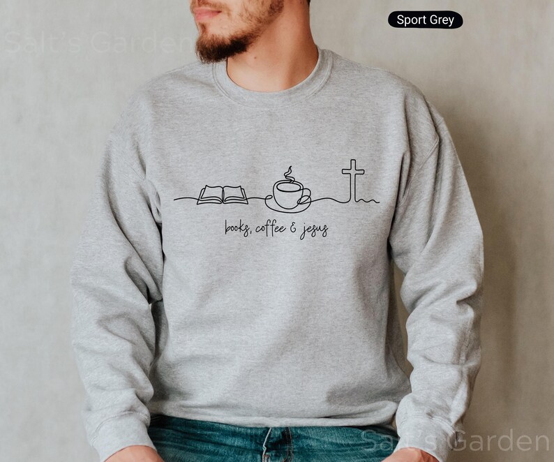 May include: Sport Grey sweatshirt with a black line art design featuring an open book, a coffee cup, and a cross, with the words "books, coffee & jesus" below. The sweatshirt is a solid light gray color.
