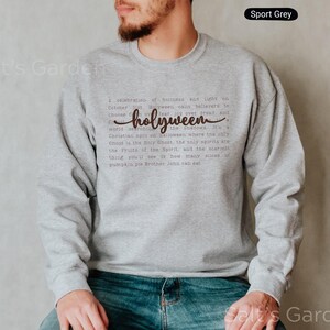 K&ouml;nnte beinhalten: Sportgraues Sweatshirt mit dem Wort "holyween" in Schreibschrift. Das Sweatshirt hat eine gedruckte Botschaft &uuml;ber Halloween. Der Text ist dunkelbraun. Das Sweatshirt ist ein lang&auml;rmeliger Rundhalsausschnitt.