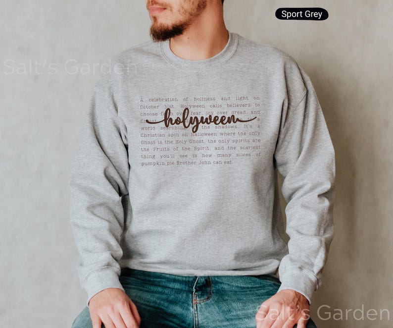 K&ouml;nnte beinhalten: Sportgraues Sweatshirt mit dem Wort "holyween" in Schreibschrift. Das Sweatshirt hat eine gedruckte Botschaft &uuml;ber Halloween. Der Text ist dunkelbraun. Das Sweatshirt ist ein lang&auml;rmeliger Rundhalsausschnitt.