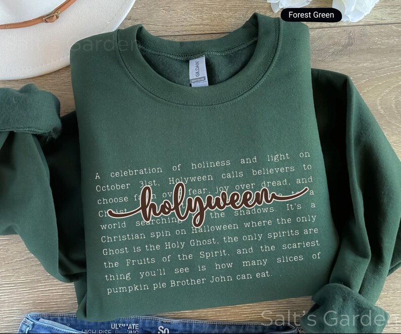 K&ouml;nnte beinhalten: Forstgr&uuml;nes Sweatshirt mit dem Wort "holyween" in Schreibschrift. Das Sweatshirt hat einen Rundhalsausschnitt und lange &Auml;rmel. Der Text auf dem Sweatshirt beschreibt eine christliche Sicht auf Halloween. Das Sweatshirt ist aus weichem Material.