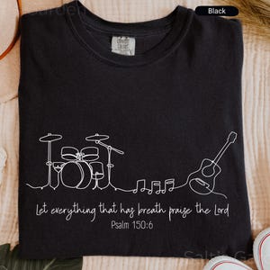 May include: Black t-shirt with a white line drawing of a drum set, guitar, and musical notes. The text "Let everything that has breath praise the Lord" and "Psalm 150:6" are also printed on the shirt.