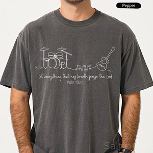 May include: Pepper-colored t-shirt with a white line drawing of a drum set, guitar, and musical notes. The text "Let everything that has breath praise the Lord Psalm 150:6" is printed below the musical instruments.