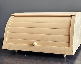 May include: A wooden bread box with a hinged lid and a small knob. The box is light brown and has a slightly rounded shape.