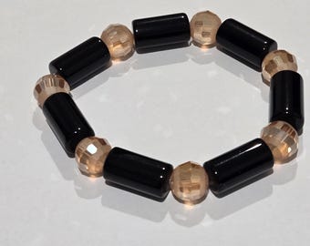 May include: A beaded bracelet featuring alternating black cylindrical beads and faceted peach-colored beads. The bracelet is displayed on a white surface, showcasing its simple yet elegant design. This accessory is suitable for everyday wear.