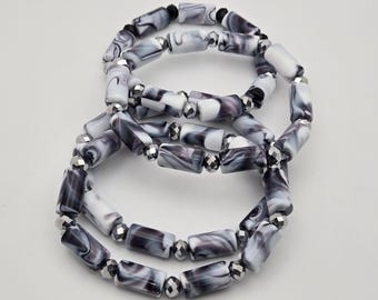 May include: Two bracelets with rectangular beads in shades of white, gray, and black. The beads have a marbled effect and are strung together with silver-colored spacer beads. The bracelets are displayed on a white surface.