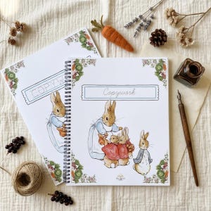 Pu&ograve; includere: Due quaderni a spirale con la scritta "Copywork" sulla copertina, con illustrazioni di conigli in abiti vintage. I quaderni sono decorati con bordi floreali e vegetali e sono accompagnati da una carota di feltro e altri elementi decorativi.