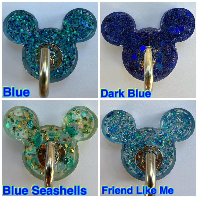 May include: Four resin wall hooks shaped like mouse heads, each featuring a metal hook. The designs include blue glitter, dark blue glitter, blue seashells with gold stars, and blue iridescent shards labeled Blue, Dark Blue, Blue Seashells, and Friend Like Me.
