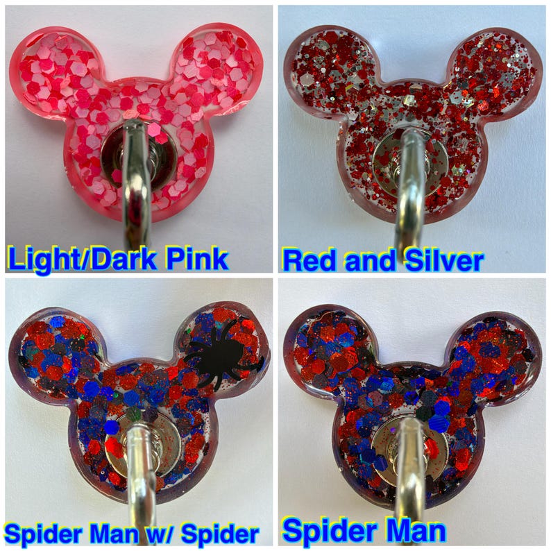 May include: Four resin badge reels shaped like mouse heads with metal clips. The top left is pink with glitter, top right is red and silver glitter, bottom left features red, blue, and black glitter with a spider, and bottom right has red and blue glitter.