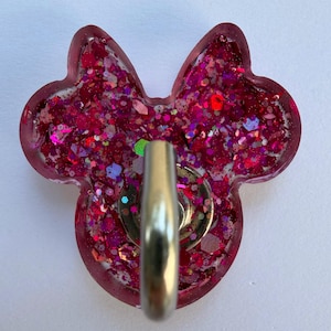 May include: A mouse-shaped badge reel featuring a translucent pink resin base filled with chunky magenta and fuchsia glitter. A circular silver metal mechanism is attached to the center of the front, providing a functional clip for identification.
