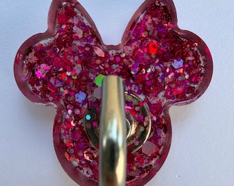 May include: A mouse-shaped badge reel featuring a translucent pink resin base filled with chunky magenta and fuchsia glitter. A circular silver metal mechanism is attached to the center of the front, providing a functional clip for identification.