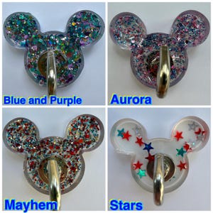 May include: Four resin wall hooks shaped like mouse heads with metal hardware. The top left is Blue and Purple glitter, top right is Aurora glitter, bottom left is Mayhem multi-colored glitter, and bottom right is Stars with red and teal star shapes.