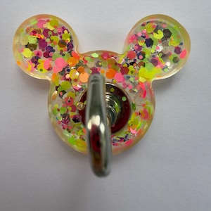 May include: A mouse-shaped wall hook made of translucent resin filled with multicolored neon glitter in shades of pink, yellow, and orange. The hook features a central silver-toned metal attachment point protruding from the center of the resin base.