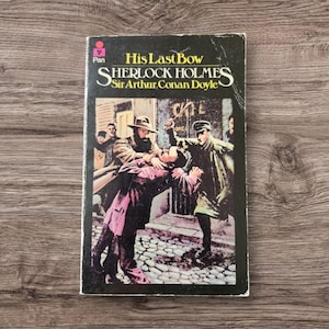 May include: Vintage paperback book titled "His Last Bow" by Sir Arthur Conan Doyle, featuring a dramatic illustration of Sherlock Holmes. The cover art depicts a scene of men in coats and hats, with a cobblestone street background.