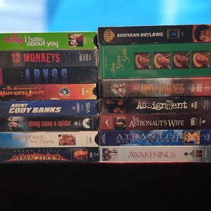 Könnte beinhalten: Ein Stapel VHS-Kassetten mit verschiedenen Filmtiteln, darunter "10 Dinge, die ich an dir hasse", "12 Monkeys", "Abyss", "American Outlaws", "Army of Darkness", "The Assignment", "The Astronaut's Wife", "Atlantis: Milo's Return" und "Awakenings".