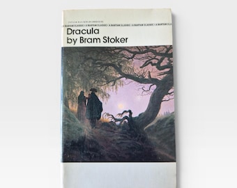 Puede incluir: Un libro de bolsillo vintage titulado "Dracula" de Bram Stoker. La portada presenta una ilustración oscura y atmosférica de figuras en un bosque con luna llena. El libro tiene lomo blanco y un aspecto desgastado.