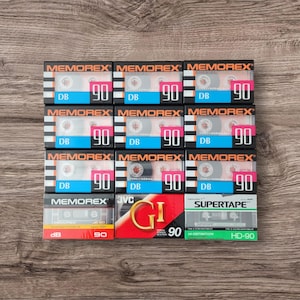 Könnte beinhalten: Eine Sammlung von zehn Audiokassetten, darunter neun Memorex DB 90-Minuten-Kassetten und eine JVC GI 90-Minuten-Kassette. Außerdem ist eine Supertape HD-90-Minuten-Kassette dabei.