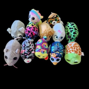 May include: A collection of small, plush animal toys in various colors and patterns. The assortment includes a gray mouse, a leopard-print creature, a rainbow-colored unicorn, a tiger, and a turtle, among others. Each toy has large, expressive eyes.