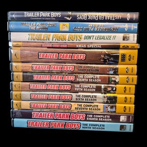 Puede incluir: Una pila de estuches de DVD de la serie de televisión "Trailer Park Boys". Los estuches, de varios colores, muestran títulos como "Countdown to Liquor Day" y números de temporada. Los DVD están apilados verticalmente sobre un fondo negro.
