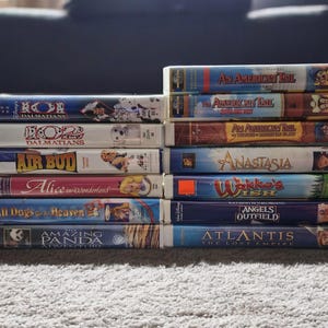 Peut inclure: Une pile de 12 cassettes VHS présentant divers films d'animation, dont "102 Dalmatiens", "Air Bud", "Alice au pays des merveilles", "Tous les chiens vont au paradis 2", "L'incroyable aventure du panda", "Un américain à Paris", "Anastasia", "Le souhait de Wakko", "Des anges dans le champ extérieur", et "Atlantide, l'empire perdu".