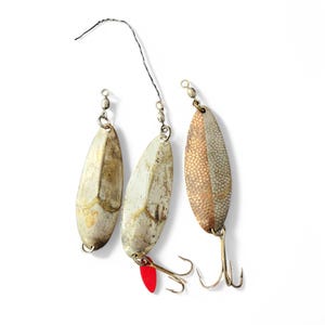 May include: Three silver fishing lures with red and gold accents. The lures are attached to fishing lines and have hooks.