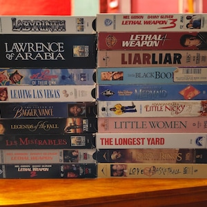 Peut inclure: Une pile de cassettes VHS avec des titres comme "Labyrinth", "Lawrence d'Arabie", "Las Vegas Parano", "Les Petites Femmes", et "Le plus long Yard".