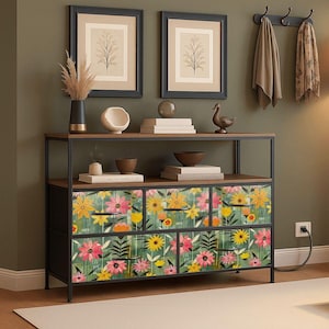 May include: A black metal and wood console table with six drawers. The drawers are decorated with a floral pattern in yellow, pink, and orange on a green background. Two framed botanical prints hang above the table.