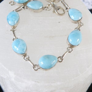 May include: A silver bracelet with light blue gemstone beads. The bracelet has a lobster clasp closure.