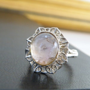 May include: A silver ring with a delicate filigree design and a large oval-shaped pink gemstone.