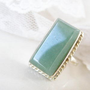 May include: A silver ring with a rectangular green gemstone set in a twisted silver band.