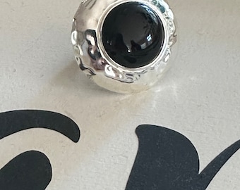 May include: A silver ring with a black gemstone set in a textured bezel. The ring has a hammered finish.