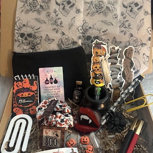 May include: A cardboard box filled with Halloween-themed stationery and accessories, including a black pouch, a notebook with ghosts, a card reading I MANIFEST MY DREAMS WITH INTENTION, MY POTION IS PASSION AND, a small cauldron, stickers, and pens.