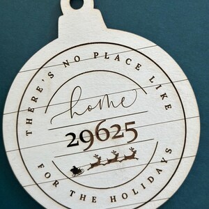 May include: A wooden Christmas ornament with the text "There's no place like home for the holidays" and the number "29625". The ornament is decorated with a silhouette of a sleigh pulled by reindeer.