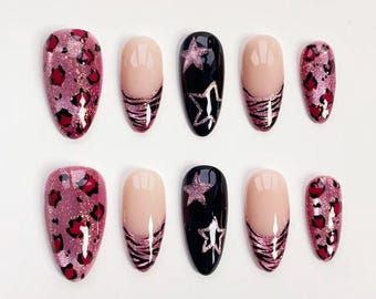 Op de afbeelding: Een set van tien kunstnagels in verschillende ontwerpen. Sommige nagels hebben een roze luipaardprint, andere hebben een nude basis met een roze glitter zebra streep, en sommige zijn zwart met een glitter ster ontwerp.