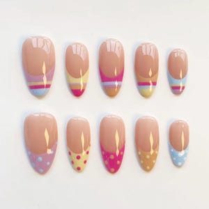 May include: A set of ten almond-shaped press-on nails featuring a nude base. The top row displays horizontal stripes in various colors, while the bottom row features polka dot patterns in matching shades of pink, yellow, blue, and tan.