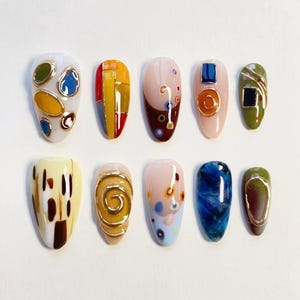 Pode incluir: Um conjunto de dez unhas postiças com designs diversos, incluindo formas coloridas com bordas douradas, listras verticais, espirais abstratas e padrões marmorizados. As unhas exibem uma variedade de cores como azul, amarelo, verde, marrom e branco, com algumas peças incorporando detalhes em dourado metálico e texturas em relevo.