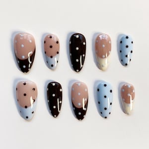 May include: A set of ten almond-shaped false nails. The nails feature a variety of designs, including solid colours, polka dots, and colour-blocked patterns. Colours include light blue, brown, and beige.