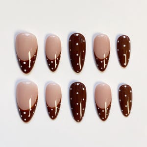 May include: A set of ten almond-shaped false nails. The nails feature a light beige base with a dark brown French tip adorned with small white polka dots. The design is consistent across all nails, offering a cohesive look.