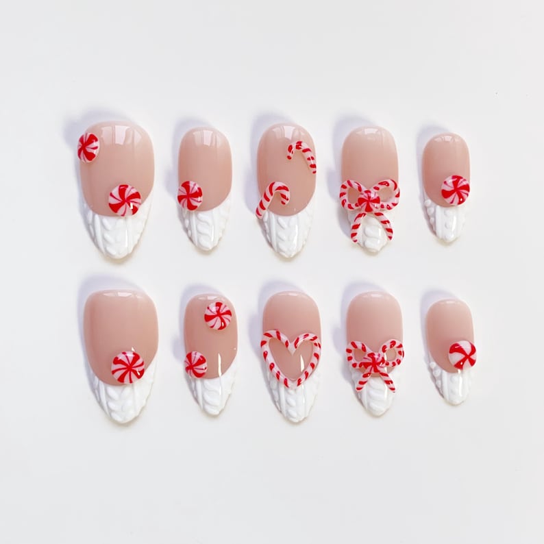 May include: A set of ten artificial nails with a light pink base and white textured tips. Each nail is decorated with red and white candy cane designs, including candy cane swirls, bows, and peppermint candies. The nails are arranged on a white surface.