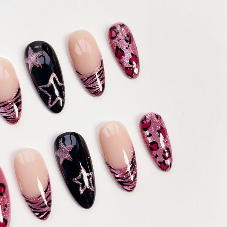 Puede incluir: Un conjunto de u&ntilde;as postizas con varios dise&ntilde;os. Algunas u&ntilde;as son negras con dise&ntilde;os de estrellas brillantes, otras son nude con rayas de cebra brillantes y otras son rosas con estampado de leopardo.
