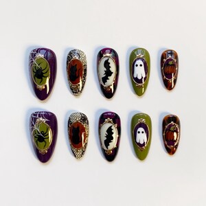 May include: A set of ten Halloween-themed press-on nails. Each nail features a different design, including a spider and web, a black cat, a bat, a ghost, and a pumpkin. The nails are oval-shaped and painted in various colors, including purple, green, and orange.