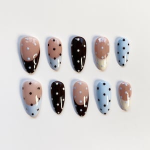 Puede incluir: Un conjunto de diez u&ntilde;as postizas ovaladas. Las u&ntilde;as presentan una variedad de dise&ntilde;os, incluyendo colores lisos, lunares y patrones de bloques de color. Los colores incluyen azul claro, marr&oacute;n y beige.