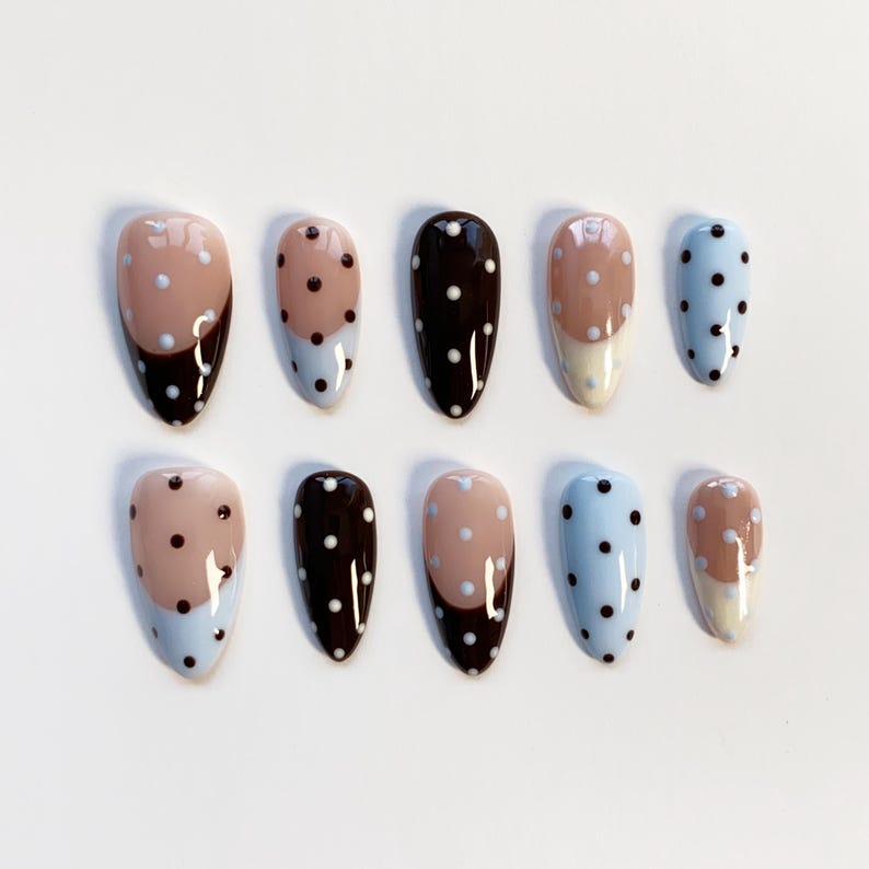 Puede incluir: Un conjunto de diez u&ntilde;as postizas ovaladas. Las u&ntilde;as presentan una variedad de dise&ntilde;os, incluyendo colores lisos, lunares y patrones de bloques de color. Los colores incluyen azul claro, marr&oacute;n y beige.