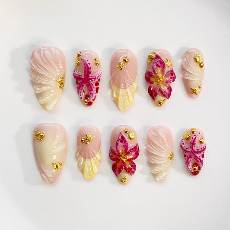 May include: A set of ten artificial nails in various designs. The nails feature a light pink base with accents of white, yellow, and gold. Some nails have starfish or flower designs, while others have textured patterns.