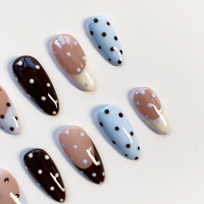 Puede incluir: Una colecci&oacute;n de u&ntilde;as postizas en forma de almendra. Las u&ntilde;as presentan varios dise&ntilde;os, incluyendo azul claro con lunares negros, marr&oacute;n con lunares blancos y nude con lunares blancos y una punta blanca.