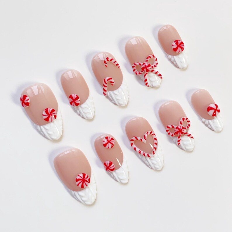 May include: Set of ten artificial nails with a light pink base and white textured tips. Each nail features red and white candy cane or bow designs, perfect for festive holiday wear.