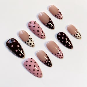 Peut inclure: Un ensemble de dix faux ongles ovales. Les ongles pr&eacute;sentent divers motifs, notamment des couleurs unies, des pois et des pointes fran&ccedil;aises. Les couleurs incluent le rose, le marron et le nude.