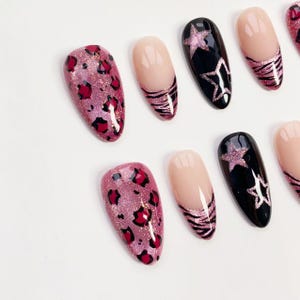 Puede incluir: Colecci&oacute;n de u&ntilde;as postizas con varios dise&ntilde;os. Algunas u&ntilde;as presentan un estampado de leopardo rosa brillante, mientras que otras tienen una base nude con rayas negras y rosas. Unas pocas son negras con una estrella rosa brillante.
