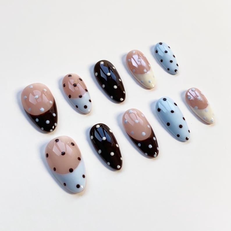 Puede incluir: Un conjunto de diez u&ntilde;as artificiales en varios dise&ntilde;os. Algunas u&ntilde;as son negras con lunares blancos, otras son de color azul claro con lunares blancos, y algunas tienen un dise&ntilde;o de dos tonos marr&oacute;n y azul claro con lunares blancos.